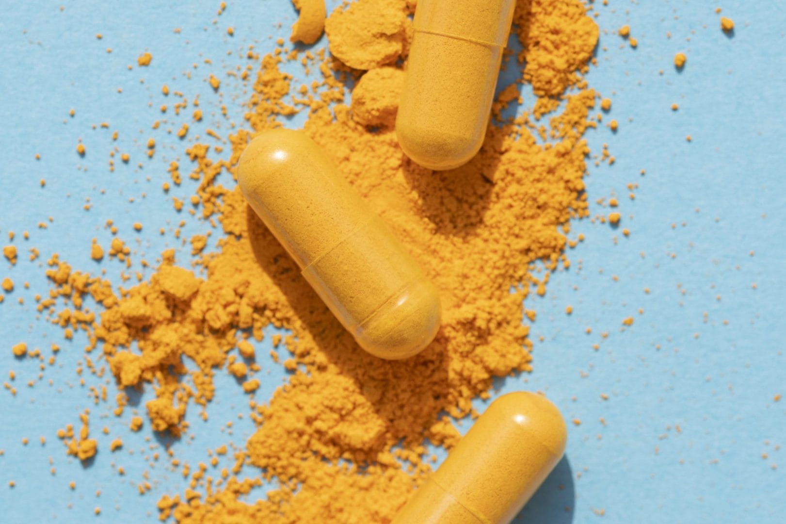 Turmeric supplement capsules and powder scattered on a blue background.