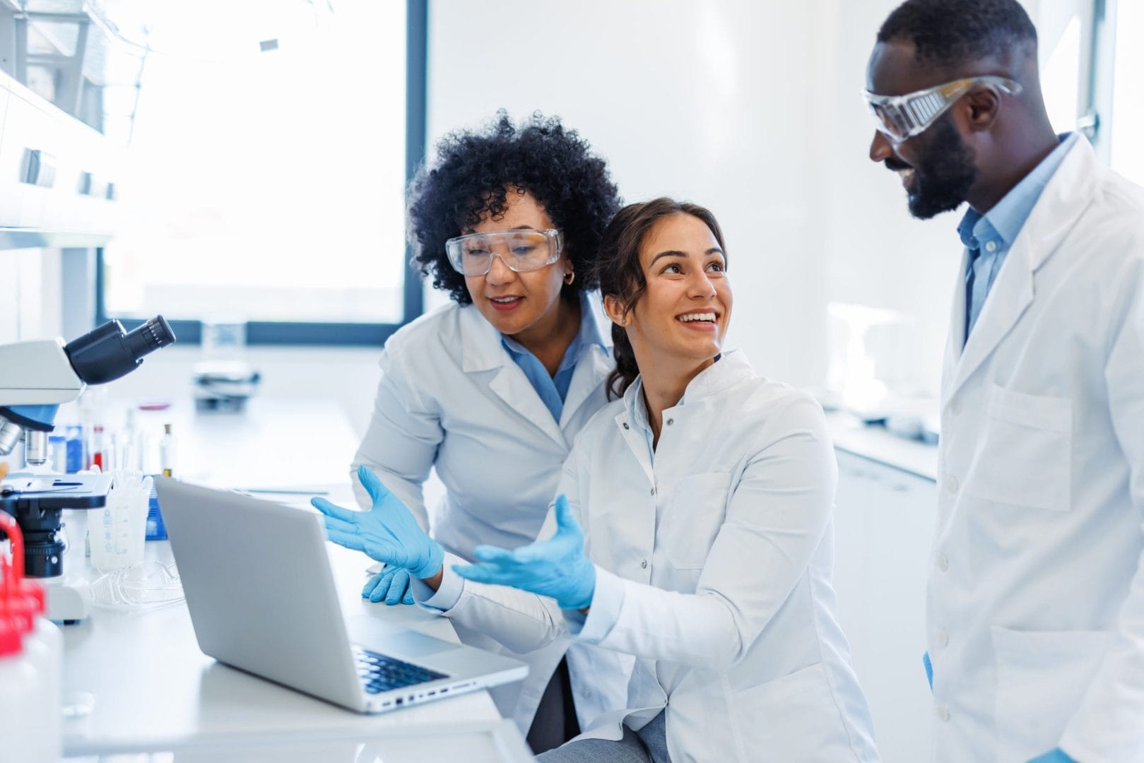 Three scientists collaborating in a modern lab, discussing supplement formulation data on a laptop.